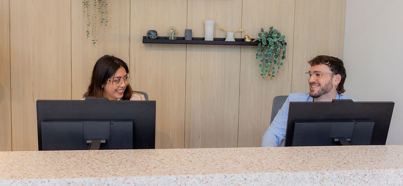 Canary Dental reception team smiling and working at front desk with modern wood panel backdrop